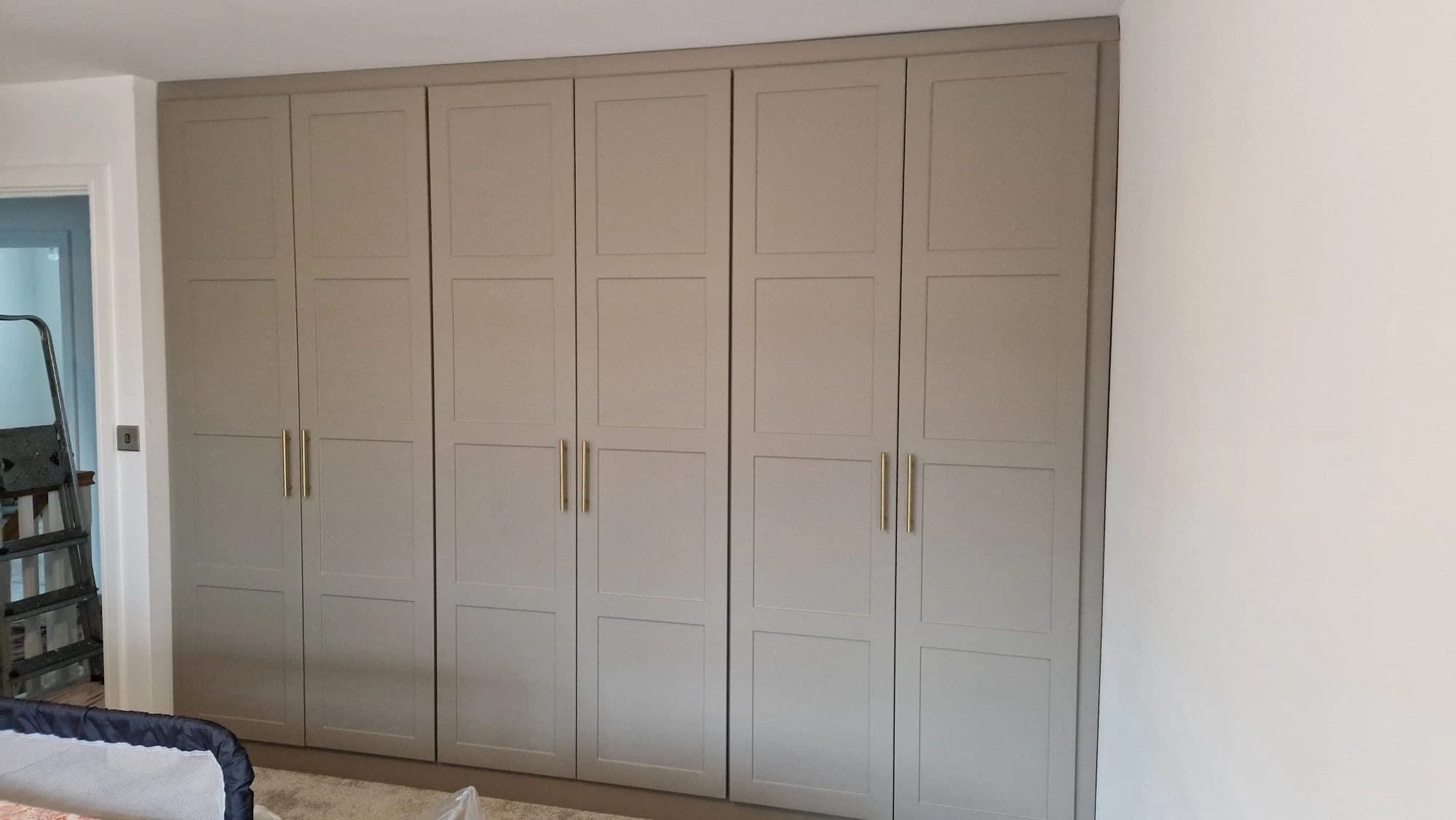Greige fitted wardrobe with square panel doors and brass handles